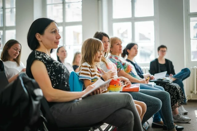 Parents and children seated in a row attentively listening during a community presentation or school event.